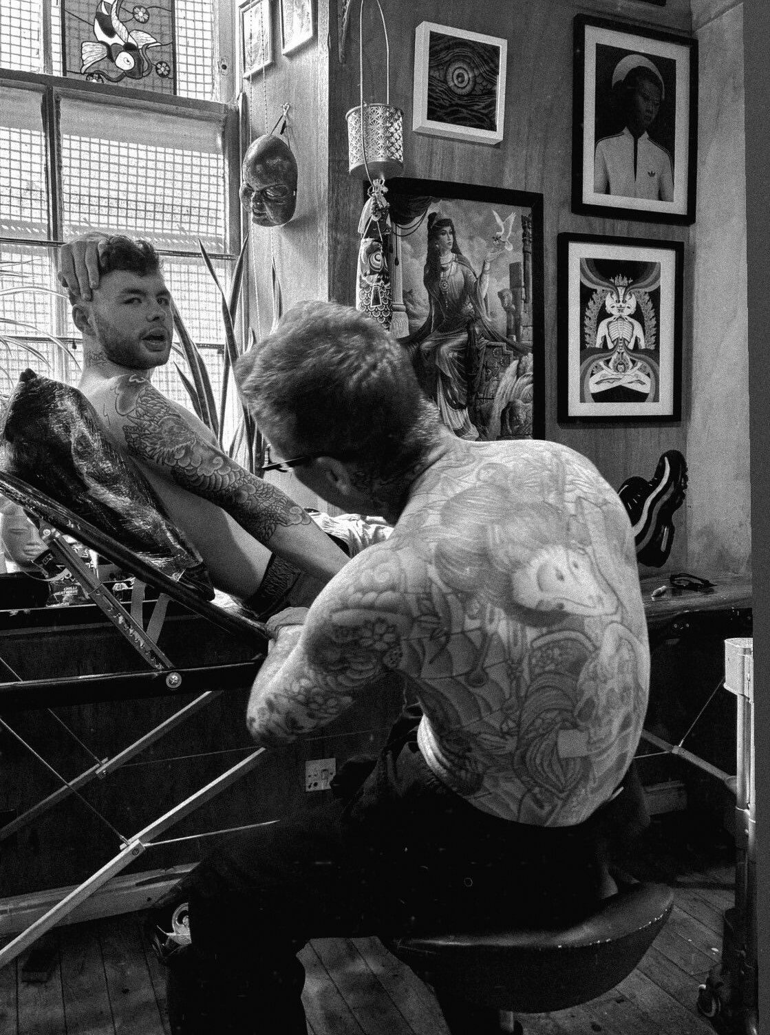 Black-and-white photograph of Roddy McLean tattooing a client in the studio